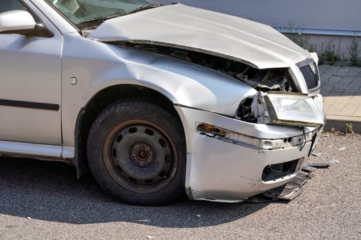 Silver car with its front crashed, plates dented and broken on asphalt road, detail to damaged part