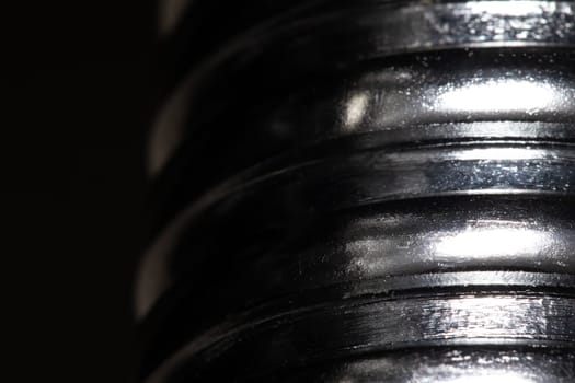 Close up of the thread of a metallic screw on black background, textured metal, abstract macro