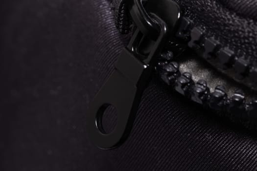 This image captures the detailed texture of a black zipper partially closed on a dark fabric, highlighting the interlocking teeth and the metal pull.