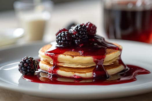 Stack of pancakes topped with blackberry maple syrup and fresh blackberries.