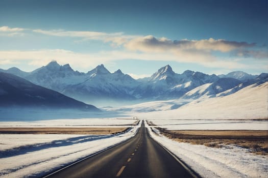 An empty road winds through a snow-covered mountain range, with the rugged peaks and snowy landscape creating a dramatic backdrop.