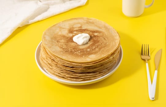 A stack of thin pancakes on a yellow table.