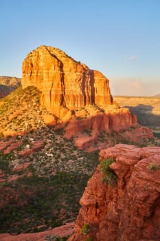Golden hour illuminates the striking strata of Bell Rock in Sedona, Arizona, contrasting the red rock formation with surrounding greenery, 2016