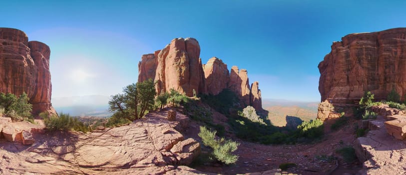 Panoramic view of towering red rock formations under a clear sky in Sedona, Arizona, showcasing the majestic beauty of the arid desert landscape.