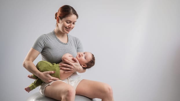 A Caucasian woman rocks her newborn son on a fitball. Copy space