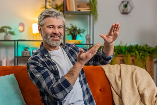 Confident rich mature man showing wasting or throwing money around hand gesture, more tips dreaming about big profit body language. Happy senior Caucasian middle-aged guy sitting on sofa in apartment