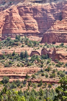 Sunlit view of the vibrant, stratified red rock formations of Devils Bridge in Sedona, Arizona, showcasing desert vegetation and geological grandeur, 2016.