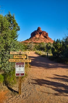 Sunny day view of majestic Bell Rock in Sedona, Arizona with a wooden trailhead sign leading towards hiking, biking and horseback riding adventures