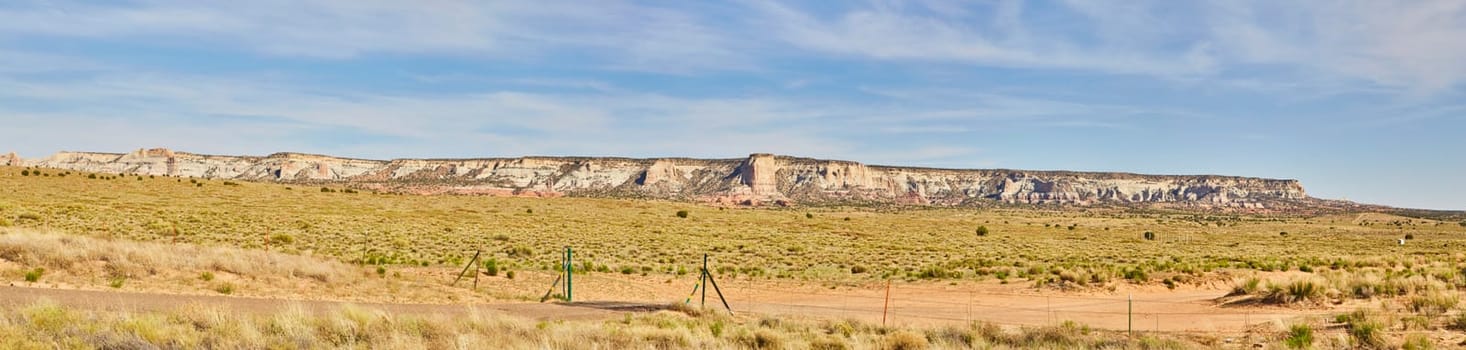 Panoramic view of majestic mesa formations under clear blue sky in Sedona, Arizona, with sparse desert vegetation and a boundary fence