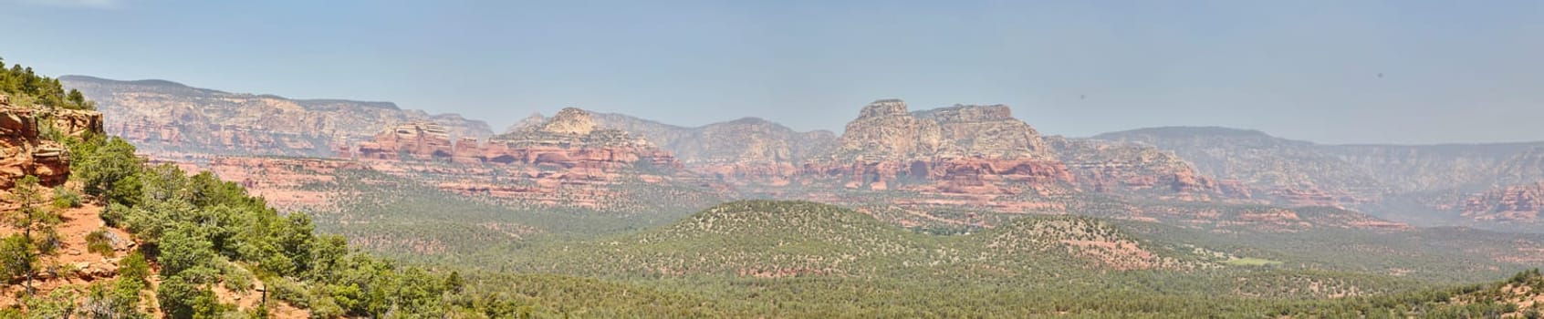 Panoramic view of Arizona's desert landscape featuring iconic red rock formations and sparse greenery under a clear blue sky in 2016, showcasing the tranquility and timeless beauty of Sedona.