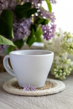 Tasty black tea in white cup on windowsill with aromatic lilac flowers. Spring composition Cup of lilac tea drinking recipe flowering branches of purple lilac. Still life for copy space greeting card, poster, banner, wallpaper. Relaxation and natural ingredients