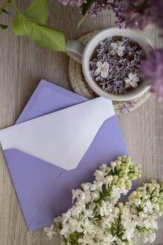 Empty envelope copy space paper note with Tasty black tea in white cup on windowsill with aromatic lilac flowers. Spring composition Cup of lilac tea drinking recipe flowering branches of purple lilac. Still life for greeting card, poster, banner, wallpaper. Relaxation and natural ingredients