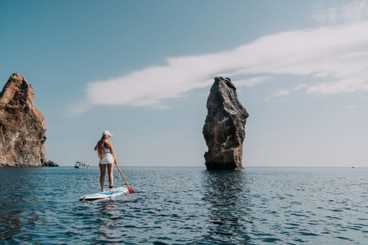 Close up shot of beautiful young caucasian woman with black hair and freckles looking at camera and smiling. Cute woman portrait in a pink bikini posing on a volcanic rock high above the sea