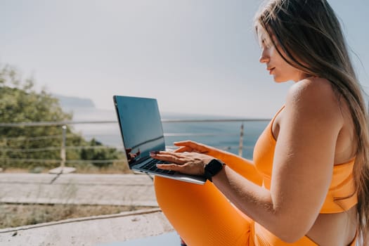 Digital nomad, Business woman working on laptop by the sea. Pretty lady typing on computer by the sea at sunset, makes a business transaction online from a distance. Freelance, remote work on vacation