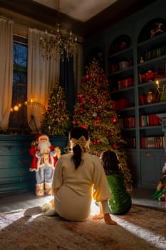 A young girl and her mother gaze at a beautifully decorated Christmas tree in their home. The room is filled with warm light, creating a cozy and inviting atmosphere.