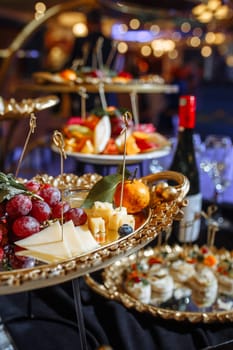 An assortment of fresh fruits, and cheeses are elegantly arranged on golden platters, creating a visually appealing and delicious display. Perfect for a party or any special occasion.