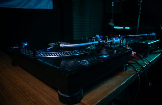 A vintage black turntable plays a vinyl record with a mesmerizing blue light in the background. It rests elegantly on a polished wooden table, creating a captivating ambiance.