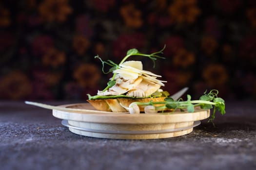 A delicious open-faced sandwich with tender chicken, melted cheese, flavorful pesto, and fresh microgreens on a wooden plate. Perfect for a quick and satisfying lunch or dinner.