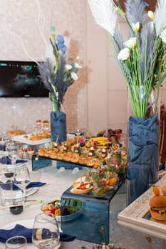 An elegant buffet table with a variety of delicious food, adorned with blue flower centerpieces and glassware, creating a sophisticated dining experience for a special event.