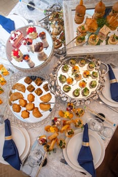 A beautifully decorated table is laden with a variety of delicious appetizers and desserts and elegantly set with white tablecloths and napkins, creating a stunning display for an elegant event.