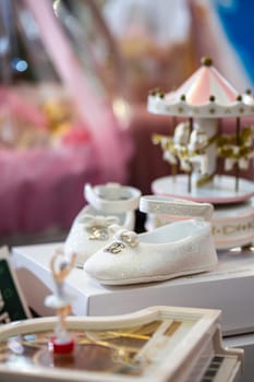 These elegant white baby shoes feature a silver glitter finish and a delicate bow accent, perfect for any special occasion. Displayed with a pink and white carousel, adding whimsy and magic.