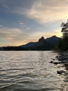 The setting sun casts a warm glow on the lake, while the rugged mountains stand tall in the background. The rocky shore is a peaceful place to relax and enjoy the view.