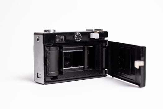 The back of a black and silver retro camera is open, exposing the film chamber. The camera is isolated on a white background, showcasing the classic design of vintage photography equipment.