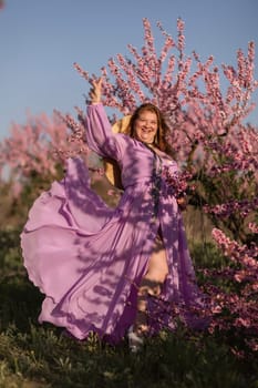 Woman blooming peach orchard. Against the backdrop of a picturesque peach orchard, a woman in a long pink dress and hat enjoys a peaceful walk in the park, surrounded by the beauty of nature