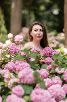 Hydrangeas Happy woman in pink dress amid hydrangeas. Large pink hydrangea caps surround woman. Sunny outdoor setting. Showcasing happy woman amid hydrangea bloom