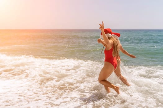 Women in Santa Claus hats run into the sea dressed in red swimsuits. Celebrating the New Year in a hot country.