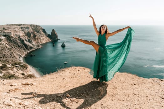 Woman green dress sea. Female dancer posing on a rocky outcrop high above the sea. Girl on the nature on blue sky background. Fashion photo