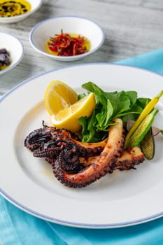 Grilled octopus with arugula and mini vegetables on a white porcelain plate