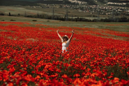 Field poppies woman. Happy woman in a white dress and hat stand through a blooming field of poppy raised her hands up. Field of blooming poppies