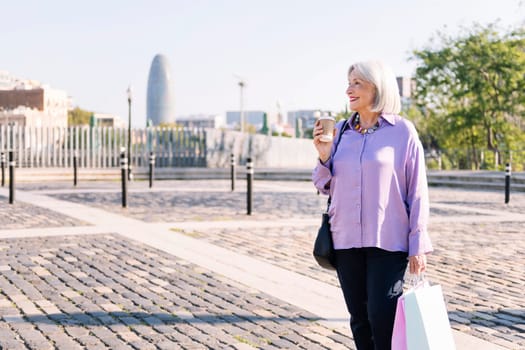senior woman smiling standing with shopping bags and a takeaway coffee, concept of elderly people leisure and active lifestyle, copy space for text