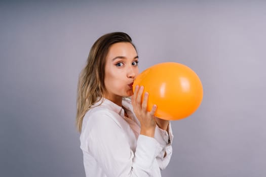 Close up portrait of young woman inflating balloon on isolated grey background