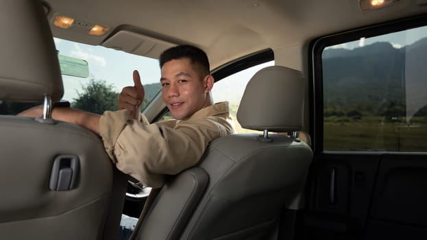 Happy young handsome man sitting inside car and showing thumbs up. Travel and active lifestyle concept.