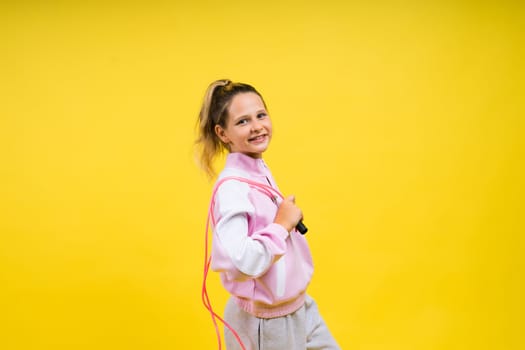 Beautiful sportsgirl with skipping rope isolated on a yellow studio