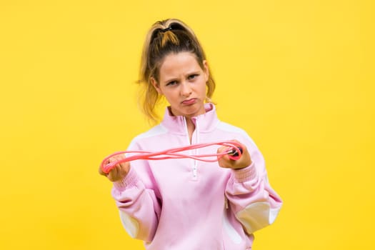 Beautiful sportsgirl with skipping rope isolated on a yellow studio