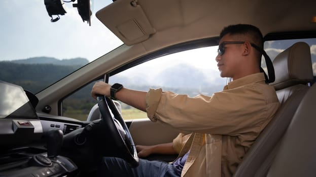 Handsome Asian male solo traveler enjoying his journey, driving car on country road.