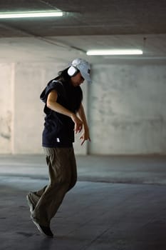 Full length of hip hop dancer listening music through wireless headphones enjoying dance in building.