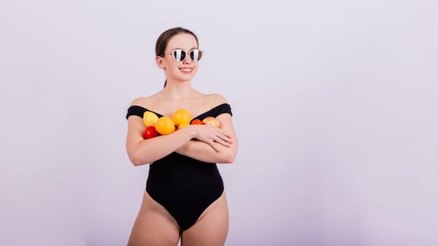 A female holding an apples, lemons, oranges in different arms isolated on grey background.