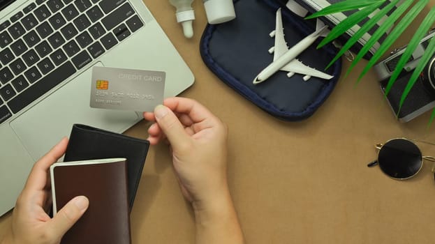 Top view of woman hand holding credit card with travel accessories and passport on desk. Traveling concepts.