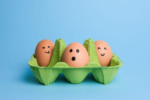 Cute easter eggs with funny faces in green box isolated on light blue background. Happy easter concept.