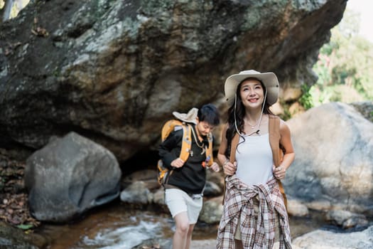 Happy LGBT Lesbian couple Travelers Hiking with Backpacks in waterfall Trail. LGBT Lesbian Couple Hikers with backpacks walks in mountains in vacation.