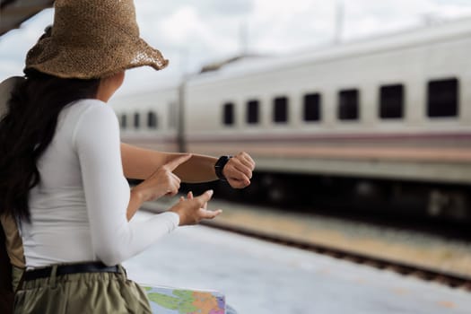 Woman traveler tourist waiting and looking at watch with map at train station. Active and travel lifestyle concept.