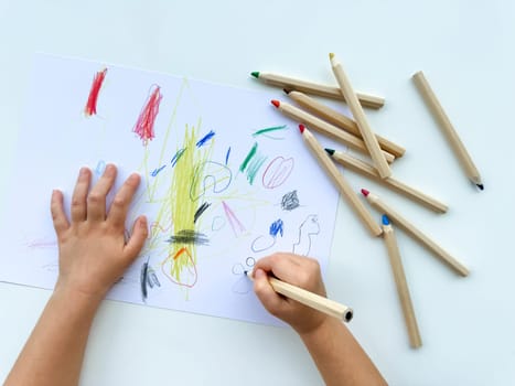 small child draws with colored pencils on paper on white table. High quality photo