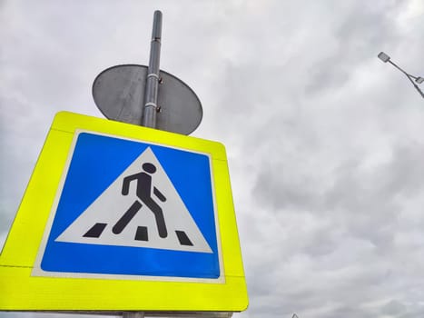 A pedestrian crossing sign on the background of a gray sky with clouds. Drawing, pictogram for pedestrians crossing the road