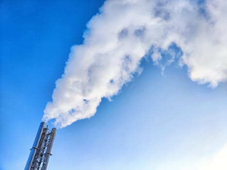 Air pollution by smoke coming out of two factory chimneys. White clouds of smoke against a blue sky background