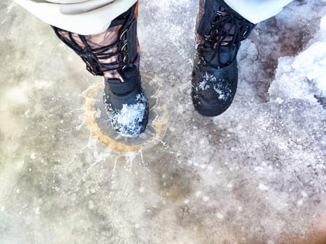 Feet of Hunter or fisherman in big warm boots on winter day on snow. Top view. Fisherman on the ice of a river, lake, reservoir on spring day with melting ice. Dangerous fishing in autumn