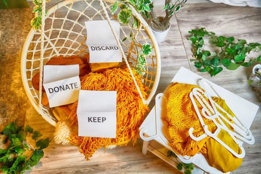 Signs with the words keep, donate, discard and fashion clothes folded in stacks in cozy room. The concept of cluttering and decluttering. Background